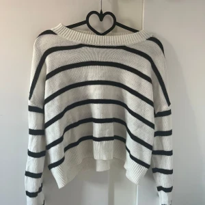 Vit och svart randig stickad tröja - Säljer en vit stickad tröja med svarta horisontella ränder. Tröjan har lång ärm, bred ribbad kant nertill och vid ärmslut samt en något lös passform. Perfekt för lager-på-lager och enkel att styla till jeans eller kjol.