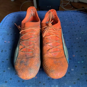 Orangea fotbollsskor från Puma ultra Elite - Säljer ett par orangea fotbollsskor från Puma med snörning och dobbar för spel på gräs. Skorna har en sportig design med inslag av silver på sidorna och är perfekta för dig som vill sticka ut på planen.