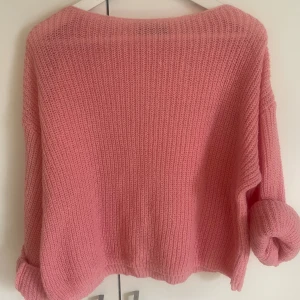 Rosa stickad tröja - Mysig rosa stickad tröja med lång ärm och avslappnad passform. Tröjan har bred halsringning och ribbade muddar vid ärmslut och nederkant. Perfekt för lager-på-lager under kyliga dagar.