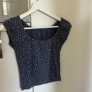 Mörkblå blommig topp från brandy Melville  - Söt mörkblå topp med små vita blommor och bred ringning. Toppen har korta ärmar och är figurnära i modellen. Perfekt för varma dagar eller somrig stil.
