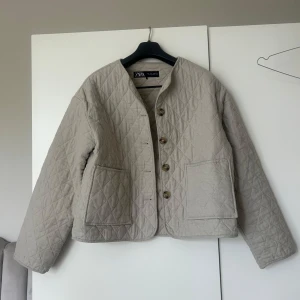 Beige quiltad jacka från Zara - Säljer denna beigea quiltade jacka från Zara med stora framfickor och knappar framtill. Jackan har lång ärm och en rak, boxig passform. Skriv vid frågor eller funderingar!