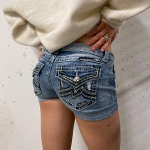 Jeansshorts från Miss Me - Snygga jeansshorts från Miss Me med coola detaljer på bakfickorna och slitningar framtill. De har en tajt lågmidjad passform midjemått tvärs över: 34cm                          Längd: 26cm                                             Benöppning: 22cm 