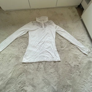 Vit långärmad tävlingsblus med spetsdetaljer - Elegant vit blus från JH collection med långa ärmar och vackra spetsdetaljer på framsidan och ryggen. Blusen har en hög krage med volang och knappar framtill. Perfekt för tävling. Nypris: 499kr mitt pris 149kr + frakt. Kontakta innan köp nu❣️