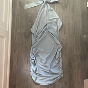 Ljusblå glittrig klänning - Snygg ljusblå glittrig klänning med oneshoulder-design och knytning i halsen. Perfekt för en festlig kväll!