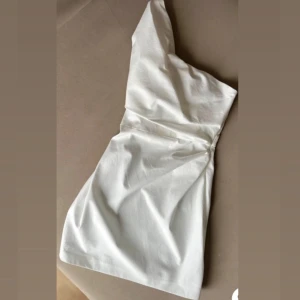 Vit axelbandslös klänning - Säljer en stilren vit klänning med en axelbandslös design. Perfekt för sommarens fester eller en elegant kväll. Klänningen har en smickrande passform och är gjord i ett lätt material.