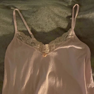 Ljusrosa linneklänning med spetsdetaljer - Säljer en söt ljusrosa linneklänning med spetsdetaljer vid halsringningen. Klänningen har smala axelband och en mjuk, flytande passform. Perfekt för varma dagar eller som ett lager under andra plagg.