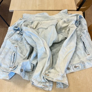 Ljusblå jeansjacka från &Denim - Säljer en ljusblå jeansjacka från &Denim. Jackan har en klassisk design med knappar framtill och två bröstfickor. Perfekt för en avslappnad stil.