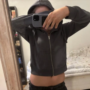 Grå hoodie från Bershka - Säljer en grå hoodie från Bershka med dragkedja och huva. Den är croppad och har långa ärmar samt en praktisk ficka framtill. Perfekt för en avslappnad stil.💗💞