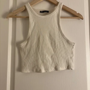 Vit ribbad linnetopp från Zara - Säljer en stilren vit ribbad linnetopp från Zara. Toppen är ärmlös och croppad, perfekt för varma dagar. Den har en enkel och klassisk design som passar till det mesta. Perfekt för att skapa en avslappnad look.