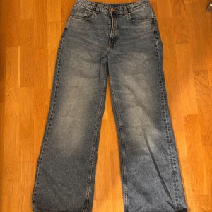 Blå jeans från H&M Divided - Säljer ett par blå jeans från H&M Divided. De har en klassisk femficksdesign och en knappgylf. Byxorna har en avslappnad passform med vida ben, perfekt för en casual look.
