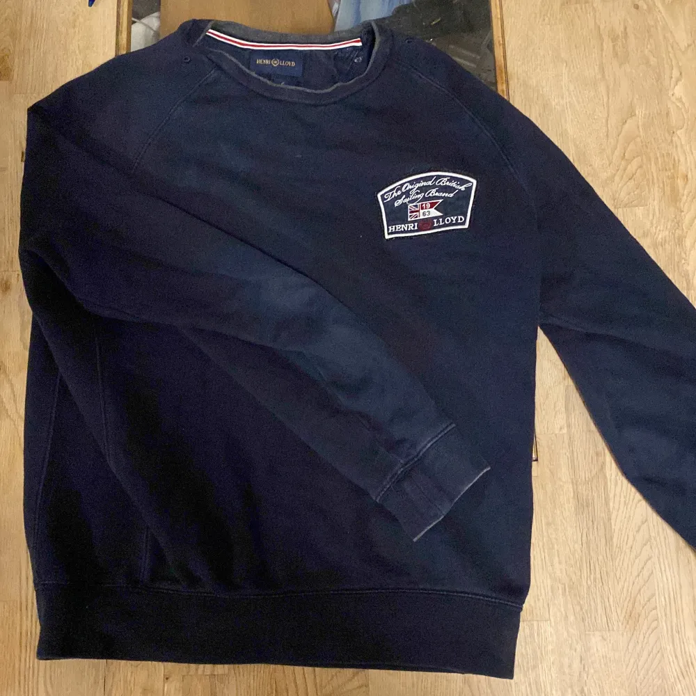 Säljer en mörkblå tröja från Henri Lloyd med ett broderat märke på bröstet. Tröjan har långa ärmar och ribbade muddar vid ärmslut och nederkant. Perfekt för en avslappnad stil.. Neuletakit & Villapaidat.