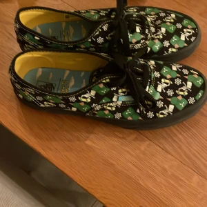 Vans x The Simpsons sneakers - Unika Vans sneakers i samarbete med The Simpsons. Skorna har ett grönt och svart mönster med karaktärer från serien och svarta snören. Innersulan är dekorerad med The Simpsons-logotypen och ett himmelsmotiv. Perfekta för fans av serien! Använda en gång 