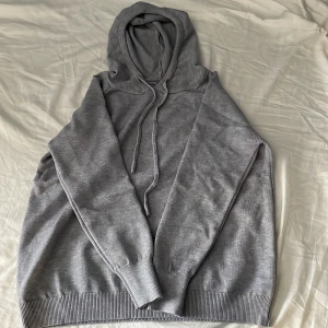 Grå merinoull luvtröja - Funkar för både tjejer och killar.Säljer en stilren grå hoodie med långa ärmar och ribbade muddar. Perfekt för en avslappnad look. Den har en justerbar huva med dragsko.