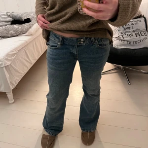 Blå jeans med bootcut - Säljer ett par klassiska blå jeans med bootcut från lager 157. De har låg midja och en snygg knappdetalj framtill. Har använt ett fåtal gånger och har inga defekter. 