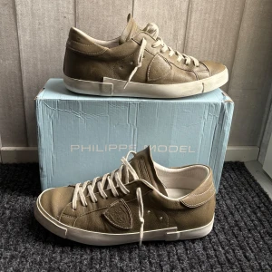 Gröna sneakers från Philippe Model - Snygga gröna skor från Philippe Model ”khaki green” med klassisk design och snörning. Skorna har en vit sula och är tillverkade i skinn, vilket ger en stilren och tidlös look. Perfekta för en avslappnad stil. Slitningar är från Philippe model skriv för fler bilder eller frågor