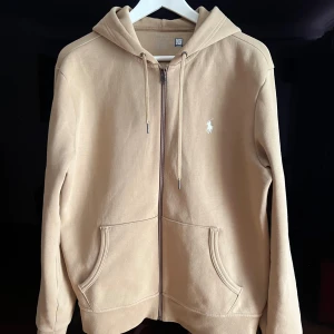 Beige zip hoodie från Polo Ralph Lauren - Säljer en stilren beige hoodie från Polo Ralph Lauren med dragkedja och klassisk logga på bröstet. Tröjan är sparsamt använd och i mycket fint skick! Ordinarie pris ca 2000.