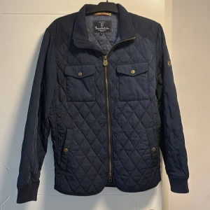 Mörkblå quiltad jacka från Bondelid - Snygg mörkblå quiltad jacka från Bondelid med dragkedja och knappar. Jackan har långa ärmar och två bröstfickor med lock. Perfekt för en stilren look. Totalt 5 fickor