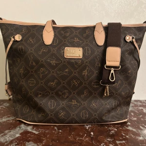 Giulia Pieralli  - Säljer en snygg brun shoppingväska från Giulia Pieralli. Väskan har en justerbar axelrem och dragkedja för säker förvaring. Väskan är i perfekt skick förutom banden som gått sönder lite..