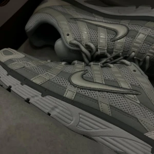 Nike P-6000 i grått och vitt HELT NYA - Snygga och sportiga Nike P-6000 sneakers i en stilren grå och vit färgkombination. Skorna har en luftig meshdesign med detaljer i syntet och klassisk snörning. Perfekta för en casual look eller träning.   Köpte fel storlek
