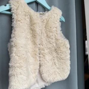 Vit pälsväst från H&M - Säljer en fluffig och mysig vit pälsväst från H&M. Perfekt för att hålla sig varm och stilren under kyliga dagar. Västen har en enkel design utan krusiduller och är lätt att matcha med olika outfits. 