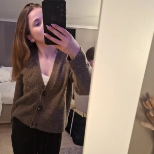 Brun stickad kofta från Lindex - Säljer en mysig brun stickad kofta från Lindex. Koftan har stora knappar framtill och ribbade muddar vid ärmslut och nederkant. 