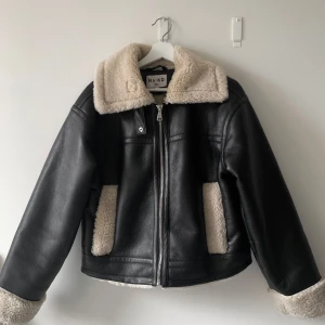 Svart skinnjacka med foder från NA-KD - Snygg svart skinnjacka från NA-KD med mjukt foder. Jackan har en dragkedja framtill och en mysig krage. Är i storlek 32, men passar mig som brukar ha 34. Använd fåtal gånger och väldigt bra skick, säljer för att den tyvärr inte kommer till användning. Kom gärna med prisförslag 💕