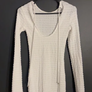 Vit ribbad klänning - Säljer en stilren vit ribbad klänning med långärmad design. Klänningen har en djup v-ringning och snörning framtill.