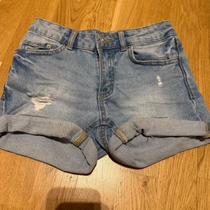Blå jeansshorts med slitningar💫 - Säljer ett par snygga blå jeansshorts med slitningar och uppvikta ben. De har en klassisk femficksdesign och knappgylf. 😮‍💨