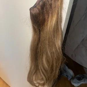 Brun hårförlängning med clips och tråd - Säljer en brun hårförlängning med clips och tråd för enkel applicering. Perfekt för att snabbt få längre och fylligare hår. Färgen är en naturlig brun nyans med subtila ljusare slingor. Medföljer 3 olika storlekar på banden. Äkta hår 