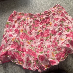 Rosa blommig kjol med volang - Charmig rosa kjol med blommigt mönster och volangdetaljer. Perfekt för en somrig look med elastisk midja för bekväm passform.