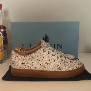Lanvin skor - Snygga sneakers från Lanvin i en unik vit och svart mönstrad design. Skorna har en brun sula och klassisk snörning. Perfekta för att ge din outfit en stilfull touch.