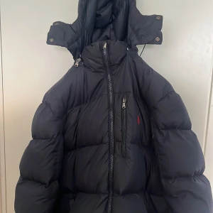 Svart dunjacka från Polo Ralph Lauren  - Säljer en svart dunjacka från Polo Ralph Lauren då det börjar att bli sommar. Det är inga stora frl med den utom att dragkedjan har tappat den lilla ringen eller vad den heter, men den funkar att använda. Pris kan diskuteras. Är det någon fråga så va inte rädd att skriva.