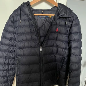 Mörkblå dunjacka från Ralph Lauren - Säljer denna feta mörkblåa Ralph Lauren jacka. Skick 8.5/10 en liten defekt att en spänna är av på ena sidan men det påverkar inte jackan så mycket. Kan tänka mig att gå ner i pris, hör av er vid frågor eller funderingar