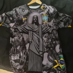 Brasil Neymar Jr. 10 special edition tröja - Unik Brasilien fotbollströja från Nike med Neymar Jr. 10 på ryggen. Tröjan har ett detaljerat svart och grått konstnärligt tryck med Kristusstatyn, brasilianska symboler och gula detaljer. Officiell CBF-logga och Nike swoosh på bröstet. Kortärmad och tillverkad i lätt funktionsmaterial.