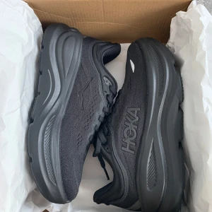 Svarta Hoka Bondi 9 sneakers - Snygga svarta Hoka Bondi 9 sneakers med chunky sula och ventilerande mesh-ovandel. Skorna har dämpad plattformssula som passar perfekt för långa promenader eller träning. Ej använda då dem är små i storleken och inte passade. Storlek: 38, Innemått: 23,5 cm