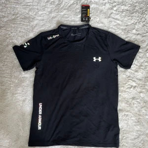 Svart Under Armour tränings-tshirt - Svart kortärmad t-shirt från Under Armour med logga på bröstet och tryck på ärmen och sidan. Tillverkad i lätt och ventilerande polyester, perfekt för träning. Snygg sportig look med rund hals och slim passform.