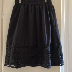 Svart långkjol från Vero Moda - Svart långkjol från Vero Moda med elastisk midja och snyggt hålmönstrad nederdel. Kjolen har en luftig passform och är tillverkad i bomullsmaterial. Perfekt för dig som gillar stilrena detaljer och vill ha en kjol med lite extra edge.