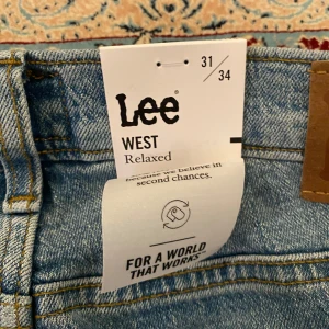 Lee West Relaxed ljusblå jeans 31/34 - Säljer ett par Lee West Relaxed jeans i ljusblå tvätt. De har en avslappnad passform med raka ben och klassiska fem fickor. Jeansen är tillverkade i bomull och har snygga kontrastsömmar. Perfekta för en chill och stilren look.