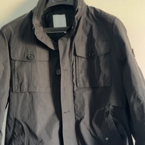 Svart vindjacka från J.Lindeberg M - Snygg svart vindjacka från J.Lindeberg, perfekt till hösten/ våren . Jackan har diskret logga på ärmen och stängs med både dragkedja och knappar. Perfekt för dig som gillar stilren och funktionell design. Nypris runt 3500/4000 kan gå ner lite i pris om det behövs 