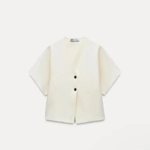 Vit v ringning väst från Zara - Stilren vit väst från Zara med v-ringning och två svarta knappar framtill. Västen har korta ärmar och rak passform, perfekt för en clean och modern look. Enkel design som passar till många outfits.