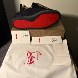 Christian Louboutin svarta sneakers mocka - Snygga svarta sneakers från Christian Louboutin i mocka med klassisk röd sula. Skorna har rund tå, svarta snören och diskreta detaljer. Insidan är beige och de har en lyxig känsla som sticker ut med den ikoniska röda undersidan.