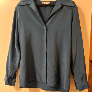 Blå silkesliknande skjorta med broderad krage - Snygg blå skjorta från Fairyset i silkesliknande material. Skjortan har långa ärmar, klassisk krage med broderade detaljer och knappar framtill. Perfekt för dig som gillar stilrena plagg med en twist. Passar till både jeans och kostymbyxor.