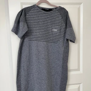 Blå/grå mönstrad t-shirt från ICIW - Snygg blå/grå träningstshirt från I can I will med diskret mönster och svarta ränder över bröstet. T-shirten har korta ärmar och en liten ICIW-logga på bröstet. Väldigt skönt material. Perfekt för en avslappnad och sportig look. Använd fåtal gånger. Passar medium/large. Nypris 699. 