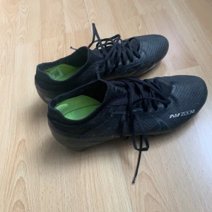 Nike Air Zoom svarta fotbollsskor strl 41 - Svarta Nike Air Zoom fotbollsskor med limegröna detaljer och sula. Skorna har snörning, låg profil och är tillverkade i syntetmaterial med textilinsida. Perfekta för dig som vill ha grymt grepp på planen och snygg stil.