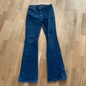 Blå bootcut jeans från Benetton - Snygga blå jeans från United Colors of Benetton med bootcut-modell och coola sömdetaljer över knäna. Klassisk femficksdesign, bälteshällor och normal passform. Perfekta för dig som gillar retrovibbar och vill sticka ut lite extra.