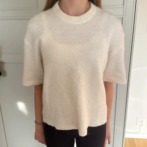 Beige stickad kortärmad tröja - En enkel och stilren beige stickad tröja med korta ärmar och rund hals. Tröjan har ribbade kanter vid hals, ärmslut och nederkant. Perfekt för lager-på-lager och funkar året runt för en chill look.