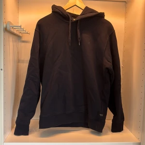 Mörk blå hoodie från Replay - En stilren mörk blåhoodie från Replay med huva och snörning. Tröjan har en klassisk passform, ribbade muddar och är tillverkad i mjuk bomull. Perfekt för en avslappnad look och enkel att matcha med jeans eller joggers.