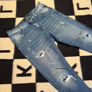 Replay MickyM slitna blå jeans - Säljer ett par ljusblå Replay MickyM jeans med slim tapered fit. Jeansen har slitna detaljer och hål på benen för en cool, avslappnad look. Klassisk femficksmodell med dragkedja och knapp. Perfekta för dig som gillar streetstyle. Storlek 30/30