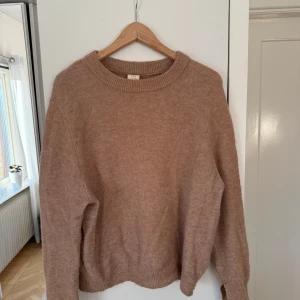 Beige stickad tröja med rund hals - Mysig beige stickad tröja från C.W med rund halsringning och ribbade muddar. Tröjan har en avslappnad passform och en diskret söm längs ryggen. Perfekt för lager-på-lager under kyliga dagar.