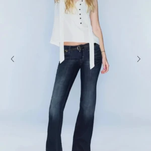 Mörkblå bootcut jeans med låg midja - Snygga mörkblå jeans med bootcut passform och låg midja. Jeansen har klassiska fem fickor, guldfärgade detaljer och markerade sömmar. Perfekta för dig som gillar en tidlös och cool look.